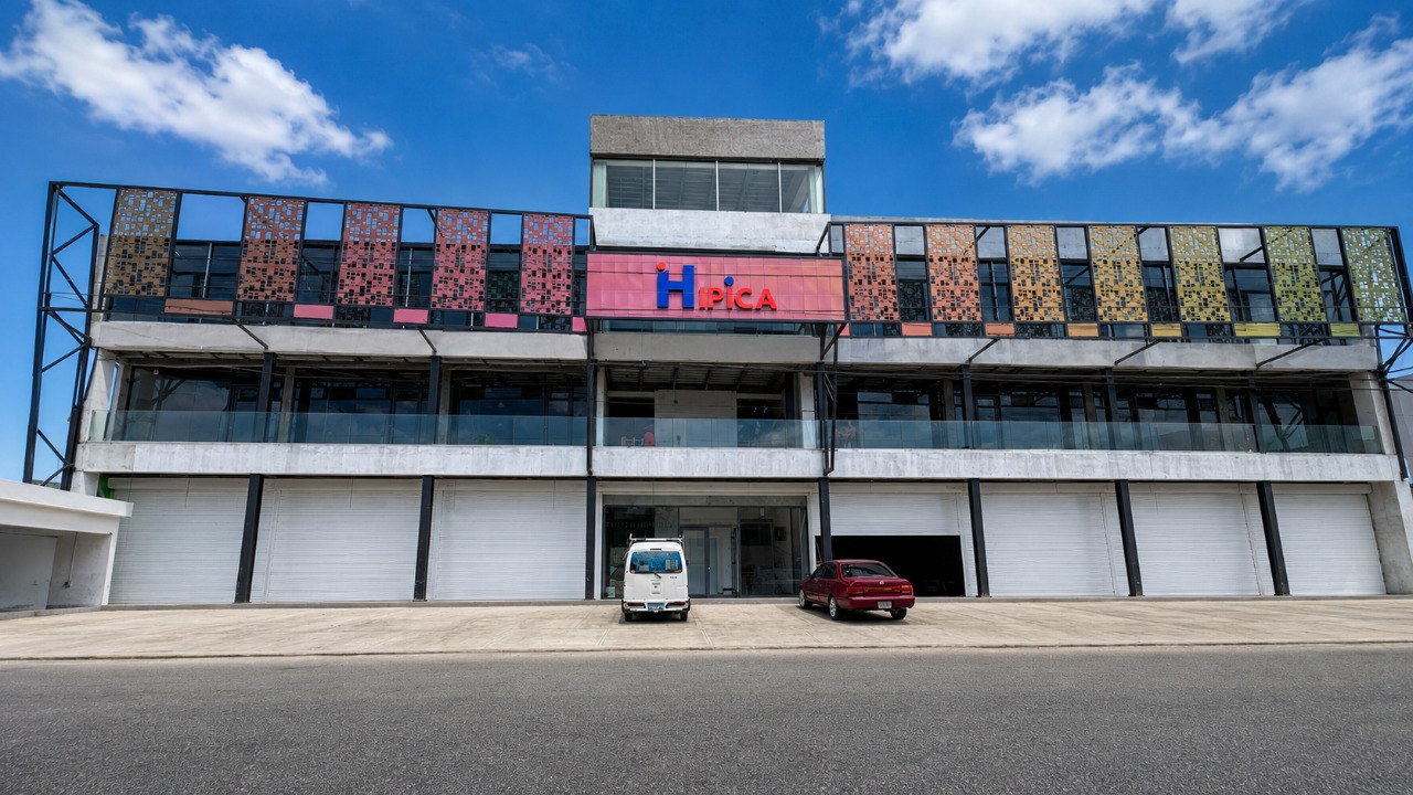 Fachada de Plaza Hípica con paneles perforados de colores y letrero corporativo