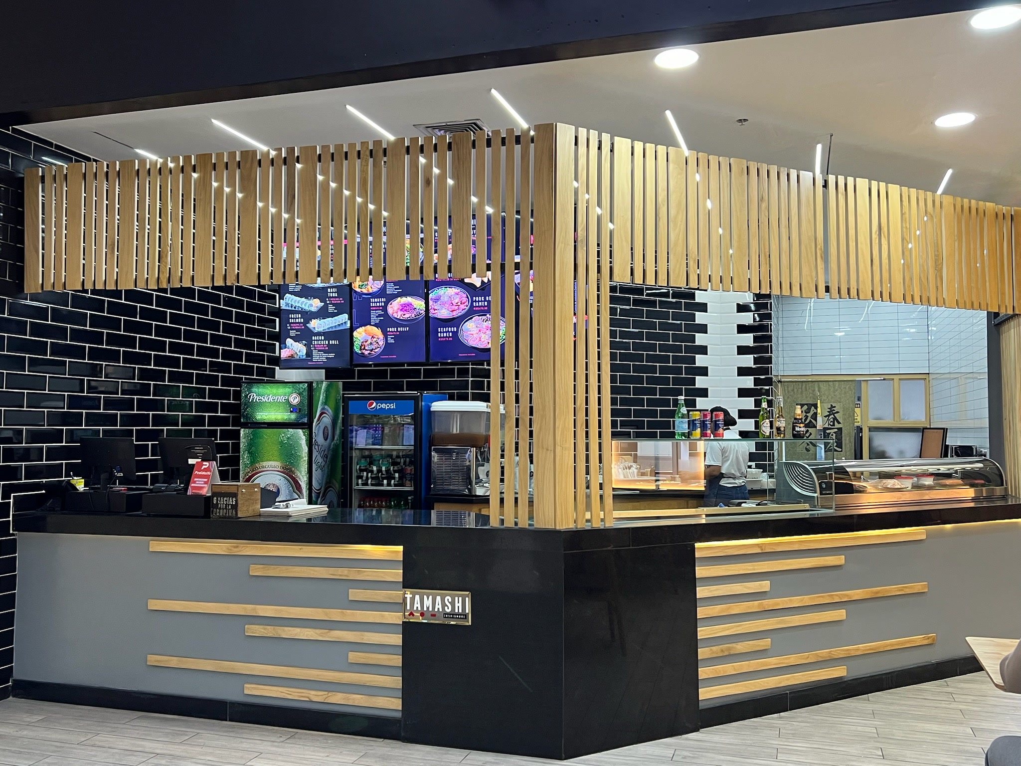 Barra de servicio con celosía de madera, azulejo negro y menús iluminados