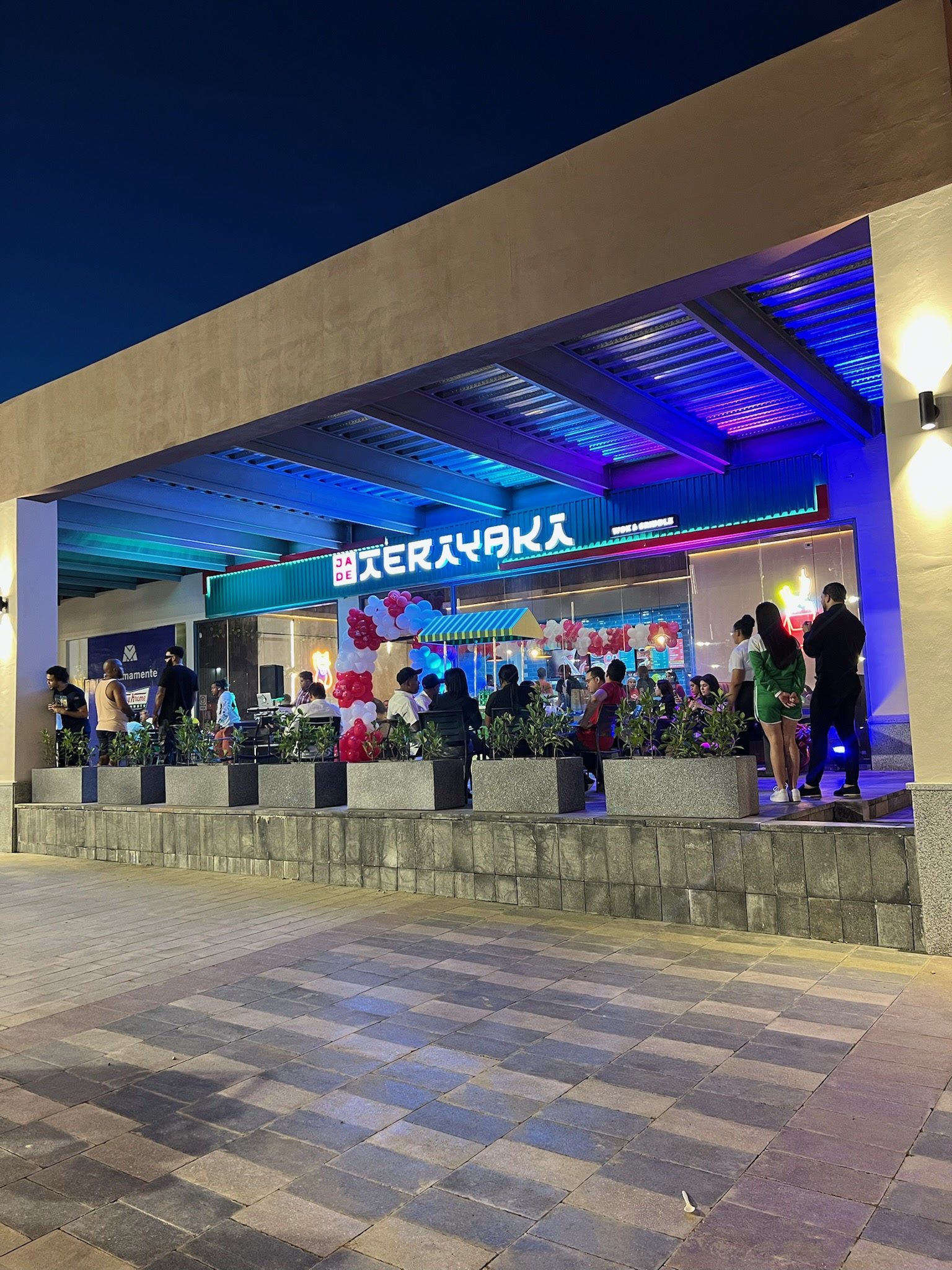 Fachada del local iluminada de noche, con terraza y jardineras