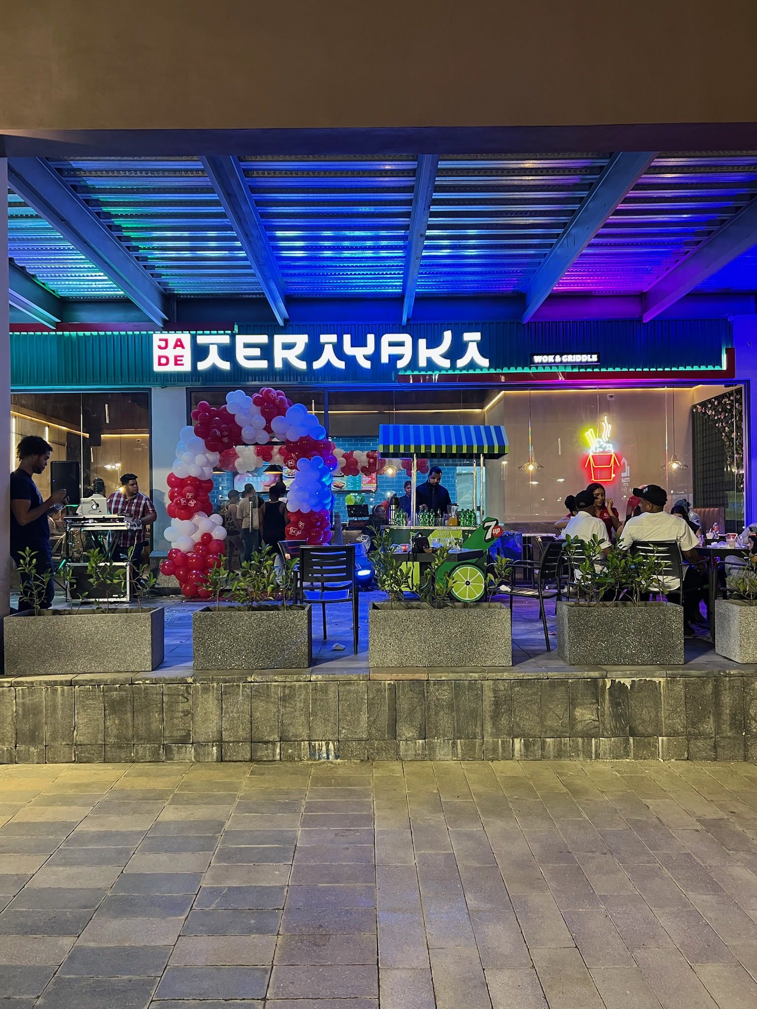 Fachada del local iluminada en apertura, con clientes en la terraza