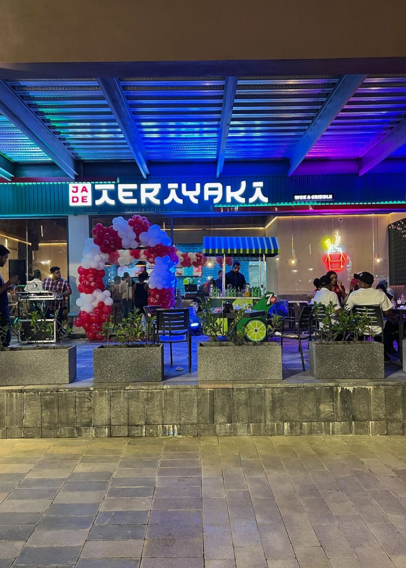 Fachada iluminada del local en su apertura, con clientes en la terraza